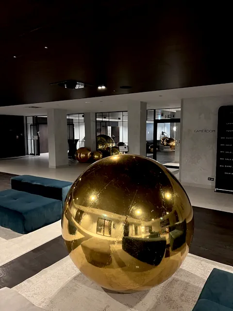 Złote dekoracje eventowe w postaci błyszczących kul w nowoczesnym wnętrzu w Warszawie, z widocznym napisem GAME ROOM, w eleganckim lobby hotelowym z zielonymi sofami