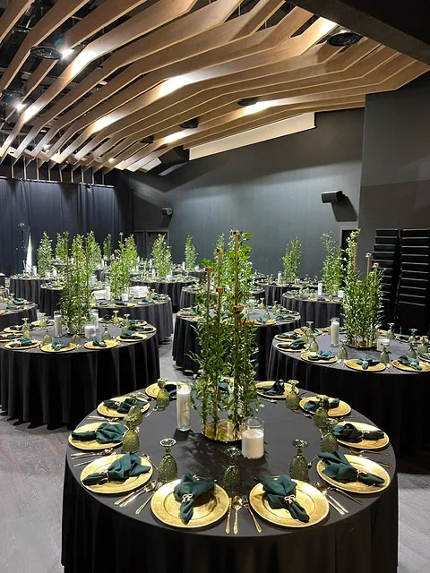 Elegancja i nowoczesność w dekoracjach eventowych w Warszawie, czarne obrusy, złote talerze, zielone serwety i delikatne oświetlenie tworzą wyrafinowaną atmosferę