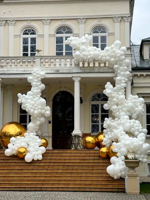 Wejście do pałacu ślubnego udekorowane białymi balonami i złotymi kulami